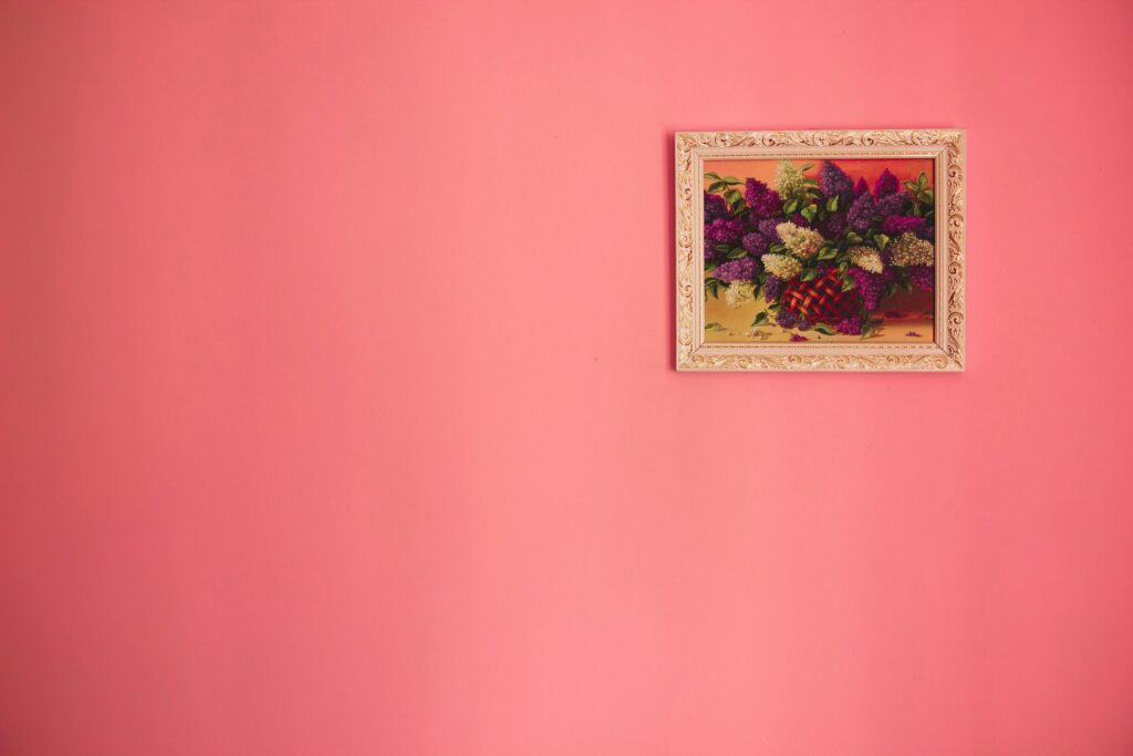 Bright floral painting in ornate frame against a pink background.